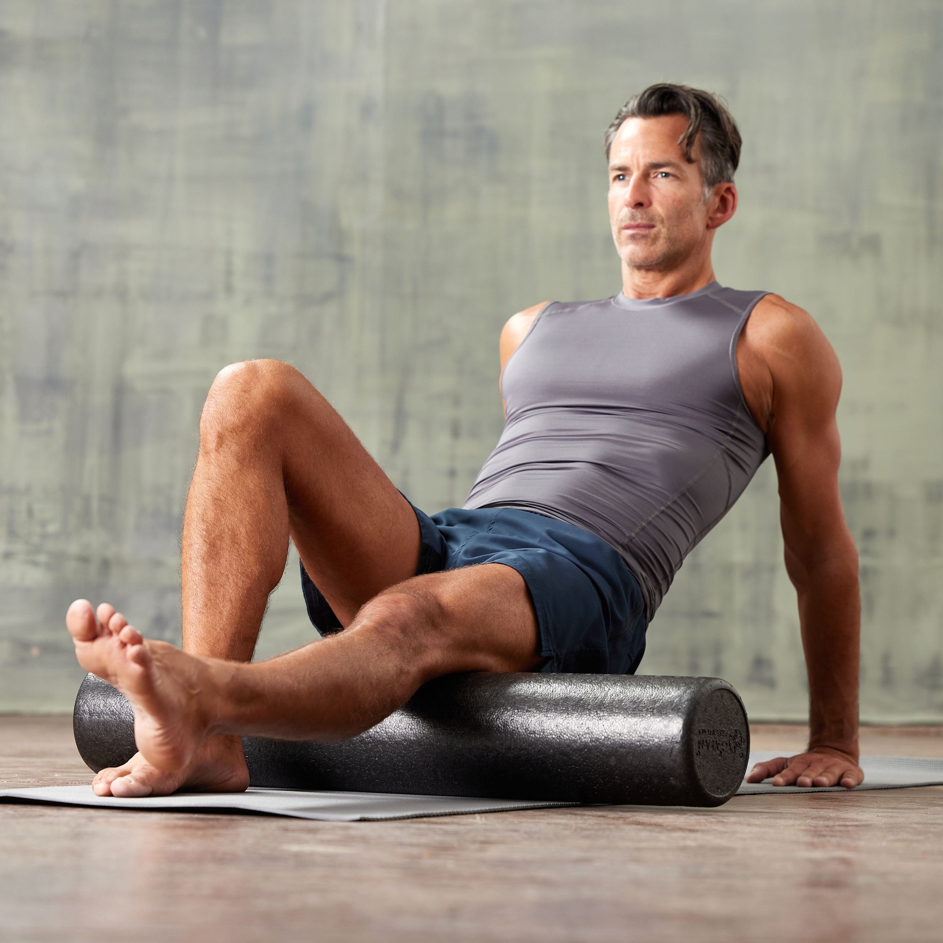 Person on the ground with the Essentials High-Density Foam Roller under the back of the upper leg